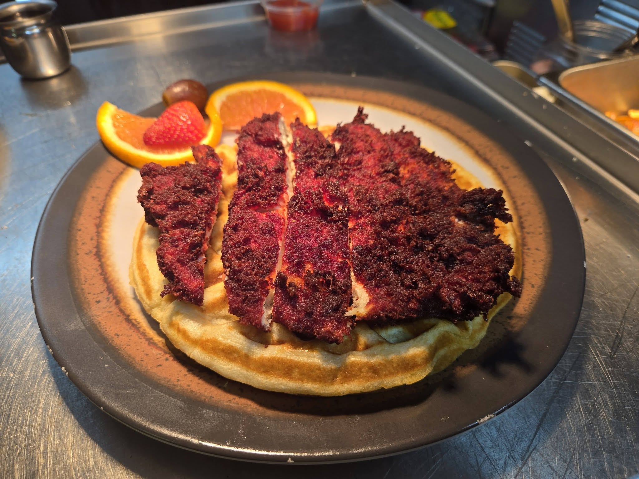 Red velvet fried chicken over a waffle with fresh fruit
